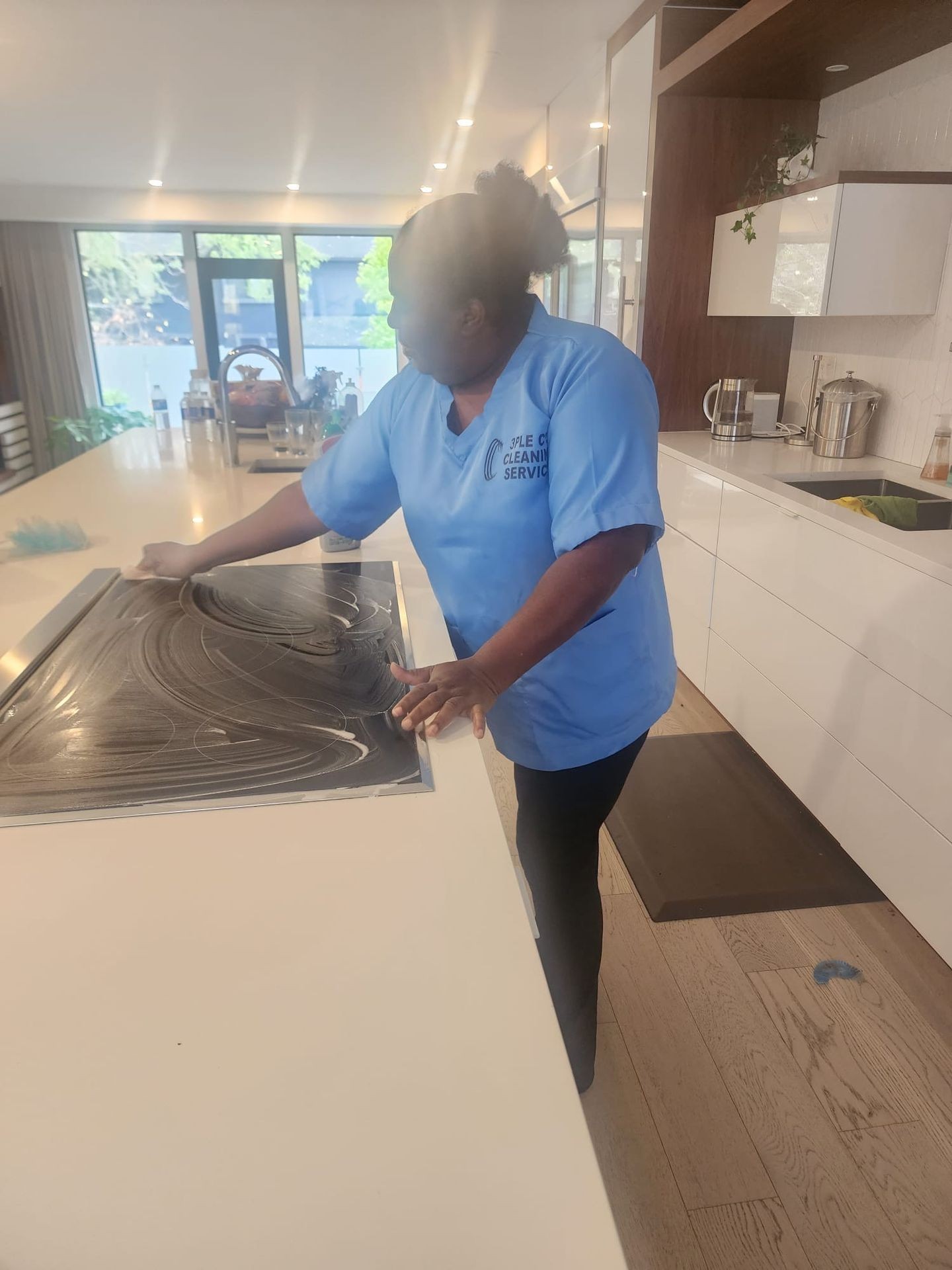Person cleaning a kitchen countertop with a cloth, standing in a modern kitchen environment.